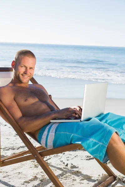 Bel homme à l'aide de son ordinateur portable tout en bronzant — Photo