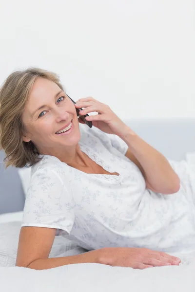 Leende blond kvinna liggande på sängen att göra ett telefonsamtal — Stockfoto