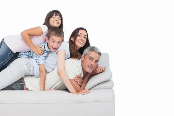 Uśmiechnięte dzieci leżąc na swoich rodziców na kanapie — Zdjęcie stockowe
