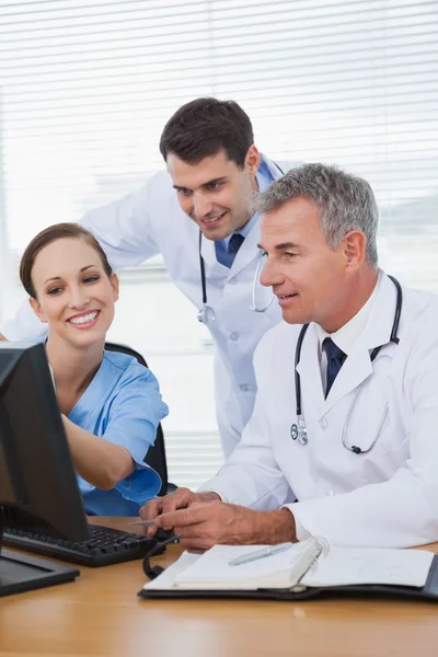 Усміхнений хірург, що працює з лікарями на комп'ютері — стокове фото
