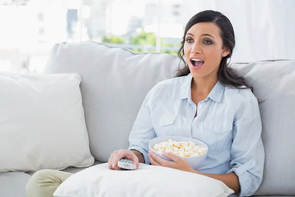 Mulher surpreendida relaxando no sofá comendo pipocas — Fotografia de Stock