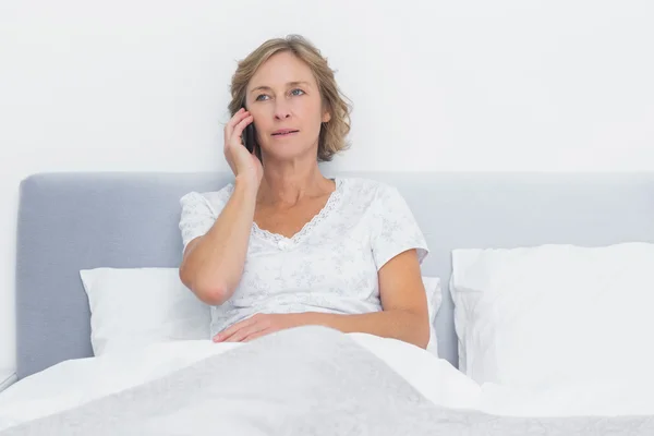 Allvarliga blonda kvinnan att göra telefonsamtal i sängen — Stockfoto