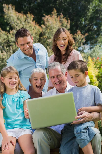 Família feliz multi geração com um laptop sentado no parque — Fotografia de Stock