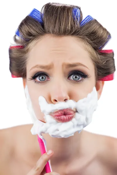 Modelo curioso em encrespadores de cabelo posando com espuma de barbear e navalha — Fotografia de Stock