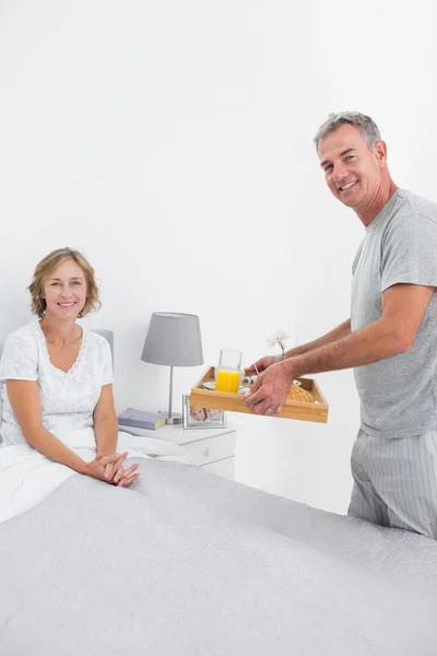 Smiling husband bringing breakfast in bed to wife — Stock Photo, Image