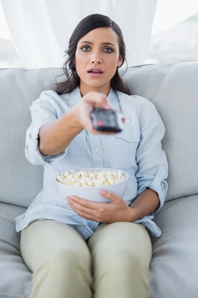 Překvapen hezká brunetka sledování televizoru a jíst popcorn — Stock fotografie
