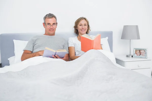 Pareja alegre sentada en la cama leyendo libros — Foto de Stock