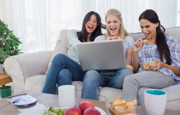 Amici sorridenti che guardano il computer portatile insieme e mangiano biscotti — Foto Stock