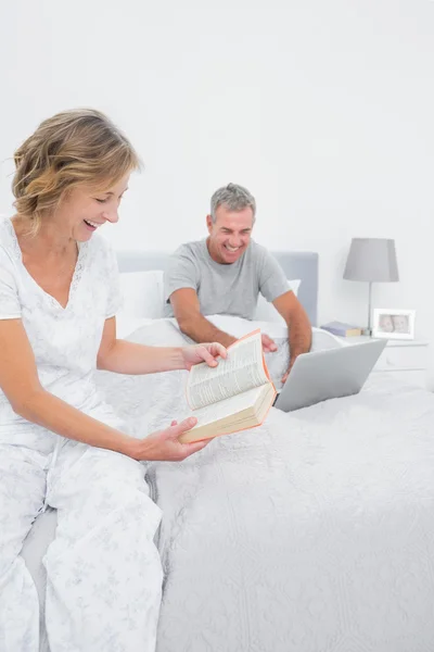 Mujer feliz leyendo libro mientras el marido está usando el ordenador portátil —  Fotos de Stock