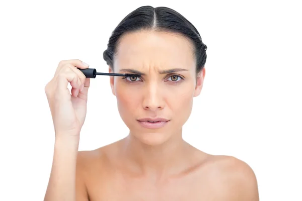 Frowning young brunette applying mascara — Stock Photo, Image