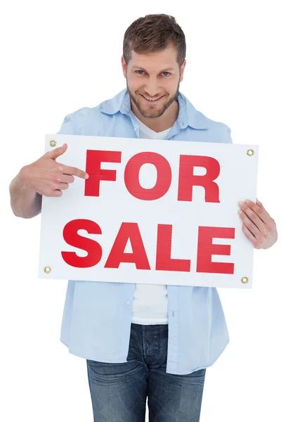 Smiling model holding a for sale sign — Stock Photo, Image