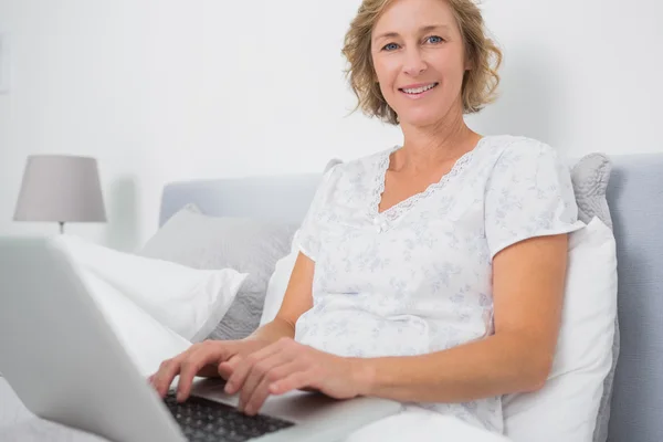 性格开朗的金发女人坐在床上使用笔记本电脑 — 图库照片