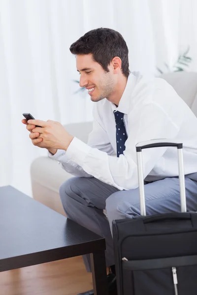 Businessman with his suitcase using mobile phone smiling — ストック写真