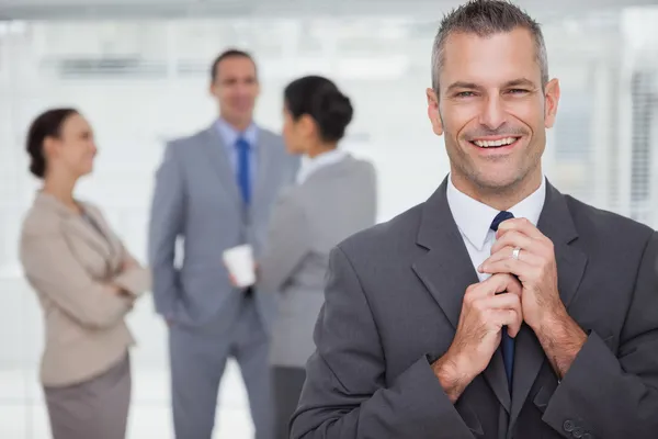 Lachende manager zijn das opruimen met medewerkers in achtergrond — Stockfoto