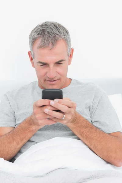 Усміхнений сіро-волохатий чоловік відправляє текст в ліжку — стокове фото