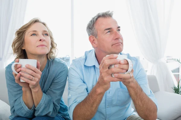 Pensativa pareja de mediana edad sentada en el sofá tomando café — Foto de Stock