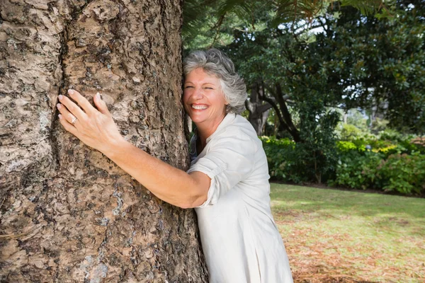 Mujer mayor sonriente abrazando un árbol — Foto de Stock