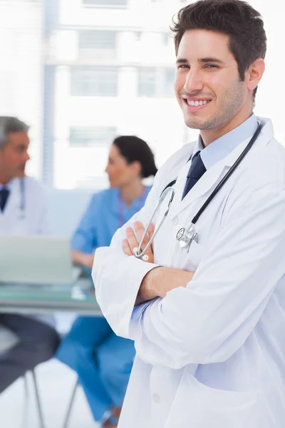 Усміхнений лікар дивиться на камеру з колегами позаду — стокове фото