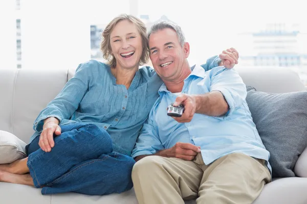 Веселая пара обнимается и сидит на диване и смотрит телевизор. — стоковое фото