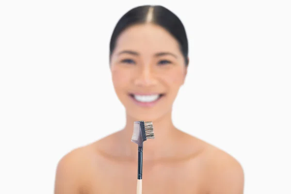 Sonriente modelo natural sosteniendo el cepillo de cejas delante de ella — Foto de Stock