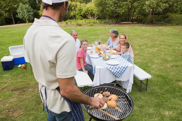 Pai de chapéu de chefs e avental cozinhando churrasco para sua família — Fotografia de Stock