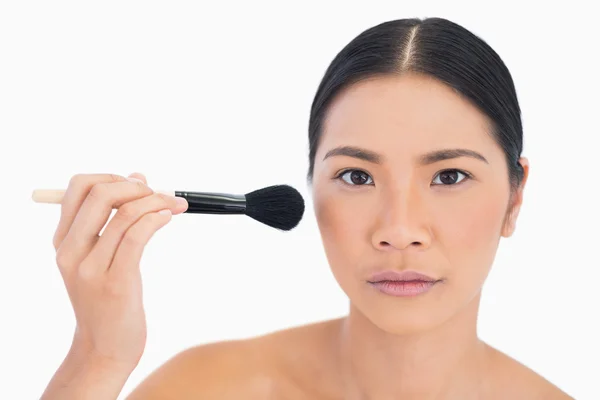 Mujer seria de cabello oscuro aplicando polvo en su cara — Foto de Stock