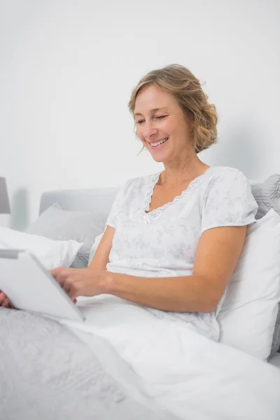 Mujer rubia feliz sentado en la cama usando tableta pc — Foto de Stock