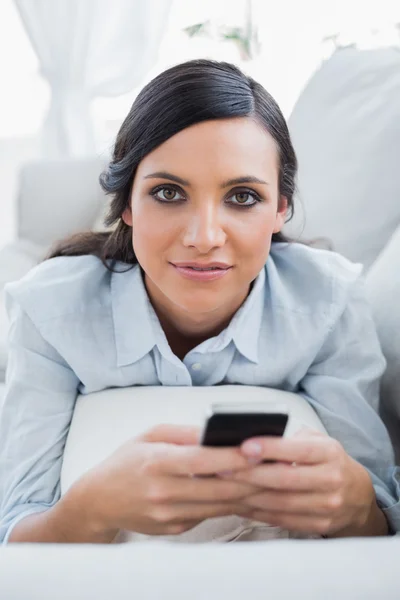 Femme aux cheveux noirs détendue allongée sur le canapé envoyant des messages — Photo