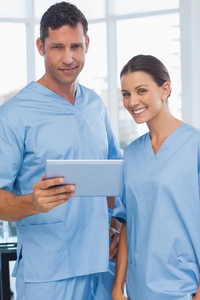 Улыбающиеся хирурги, работающие вместе над планшетом — стоковое фото