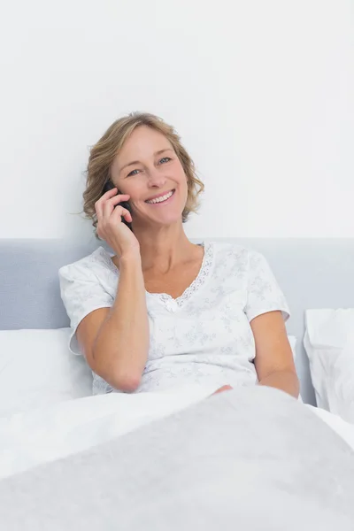 Gelukkig blonde vrouw aan de telefoon bij het bed glimlachen op camera — Stockfoto