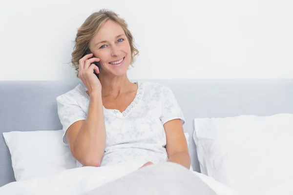 Blonde vrouw aan de telefoon bij het bed glimlachen op camera — Stockfoto