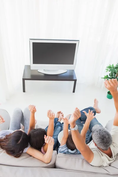 Family sitting on sofa cheering in front of television — Stock Photo, Image