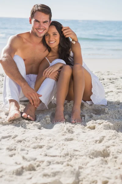 Paar umarmt lächelnd in die Kamera auf Sand sitzend — Stockfoto