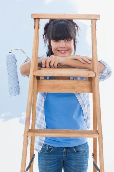 Mulher feliz segurando rolo de pintura inclinada na escada — Fotografia de Stock