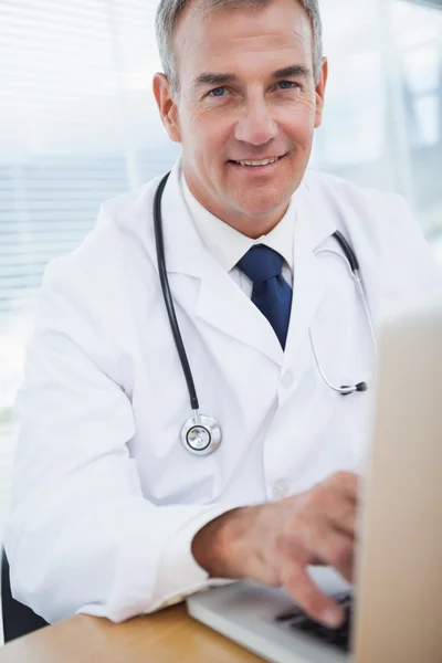 Lächelnder erfahrener Arzt tippt auf seinem Laptop — Stockfoto