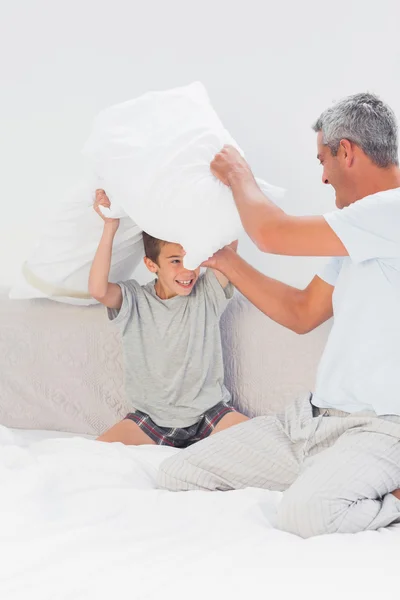 Отец и сын сражаются вместе с подушками на кровати — стоковое фото