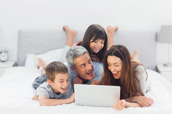 躺在床上使用其便携式计算机上的快乐家庭 — 图库照片