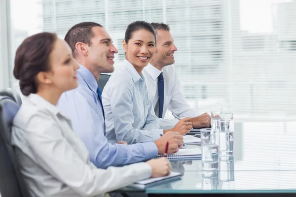 Empresaria sonriendo a la cámara mientras sus colegas escuchan —  Fotos de Stock