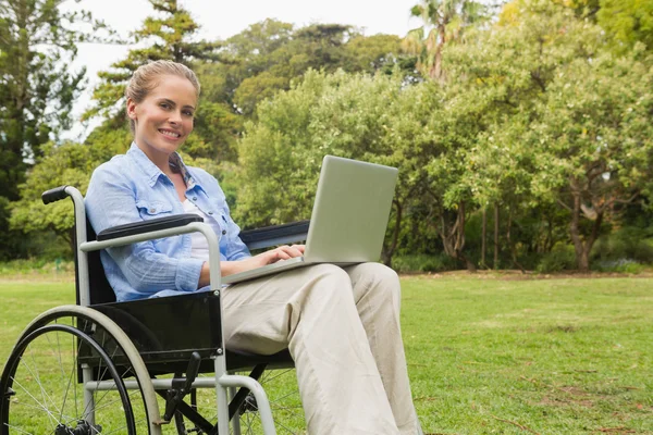 Femme souriante dans un fauteuil roulant avec un ordinateur portable — Photo