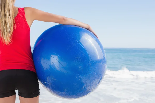 Fit blonde holding exercise ball looking at waves — Stock Photo, Image