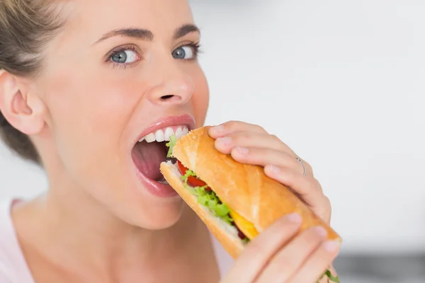 Happy woman eating sandwich and looking at camera — Stock Photo, Image