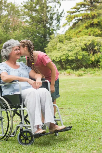 Neta beijando bochecha da avó em cadeira de rodas — Fotografia de Stock