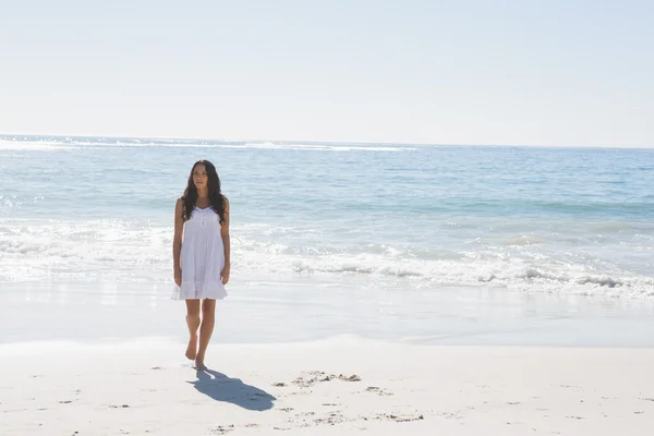 Брюнетка в белом платье, идущая от моря — стоковое фото