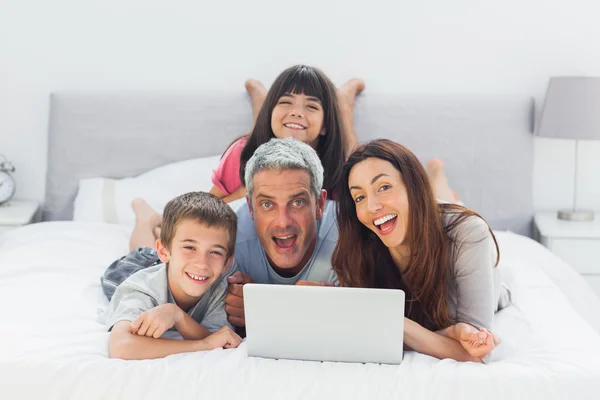 Divertida familia acostada en la cama usando su computadora portátil — Foto de Stock