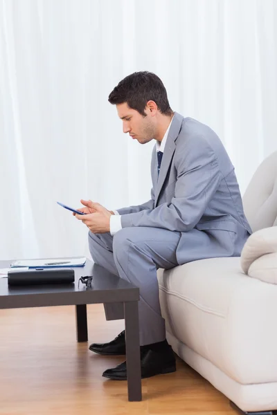 Бизнесмен, сидящий на диване и переписывающийся со своим мобильным — стоковое фото