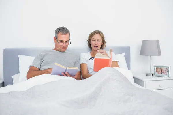 Casal feliz sentado na cama lendo livros — Fotografia de Stock