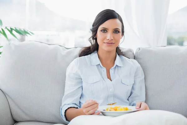 Pretty woman sitting on the couch eating fruit salad — Stock Photo, Image