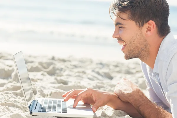 Szczęśliwy przystojny mężczyzna na plaży przy użyciu jego laptop — Zdjęcie stockowe