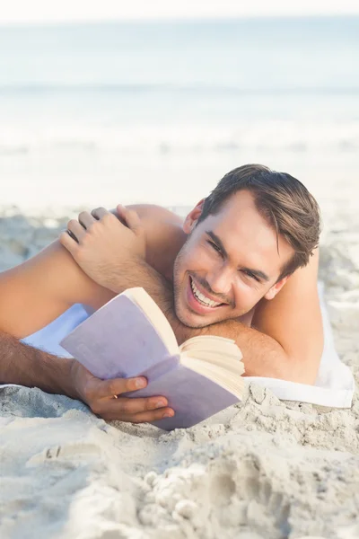 Lächelnder schöner Mann am Strand, der ein Buch liest — Stockfoto