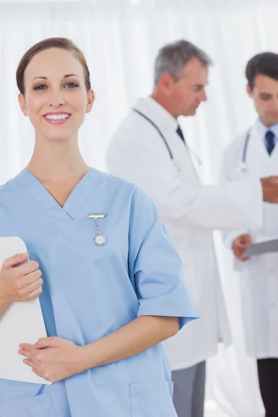 Cheerful surgeon posing while doctors talking on background — Stock Photo, Image